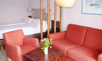 A modern room with a double bed and a cozy red sofa. A small table with a flower vase creates an inviting atmosphere.