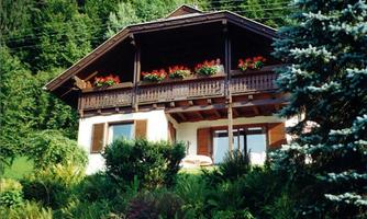 A beautiful wooden house with a balcony and blooming flowers. It is surrounded by lush greenery.
