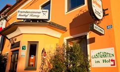 An inviting inn with an orange facade and a well-kept entrance area. The sign points to a guest garden in the courtyard.