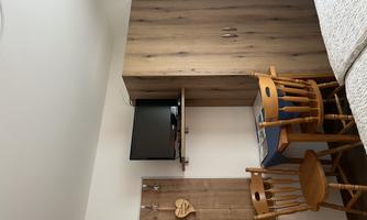 A simple room with two beds, a table, and two chairs. On the wall, there is a television and a wooden shelf with hooks.