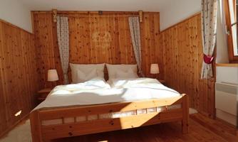 A cozy bedroom with wooden walls and a large double bed. There are two nightstands with lamps and windows with curtains.