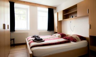 A cozy bedroom with a double bed and wooden wardrobes. The windows let in plenty of daylight and the decoration is simple and modern.