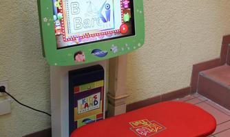 A colorful interactive play device for children is positioned against the wall. It features a screen and a matching bench in bright colors.