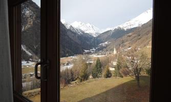 A picturesque view from a window of the snow-covered mountains. In the valley lie meadows and a small village.