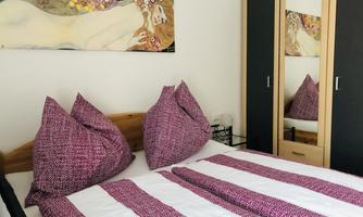 A cozy bedroom with a double bed and purple striped pillows. A piece of artwork hangs on the wall and a mirror reflects the room.
