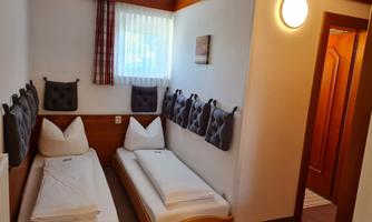 A cozy room with two single beds and bright walls. There is a large window that lets in daylight.