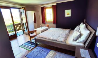 A cozy bedroom with a large bed and colorful carpets. There is a balcony with a view and a small table for two people.