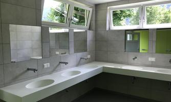 A modern bathroom with large windows and gray tiles. There are multiple sinks and large mirrors.