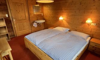 A cozy wooden bedroom with a double bed and warm lighting. On the wall hang a mirror and two nightstands.