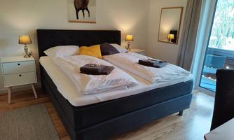 A cozy bedroom with a large double bed and stylish nightstands. The warm lights create an inviting atmosphere.