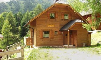 A cozy wooden house in a green mountain landscape. Surrounded by trees and gentle hills.