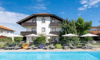 A modern building with a swimming pool and sun loungers. Surrounded by trees and a clear blue sky.