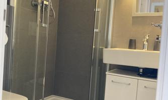 A modern bathroom with a shower cubicle and a sink. The walls are painted in neutral colors and there is stylish lighting.