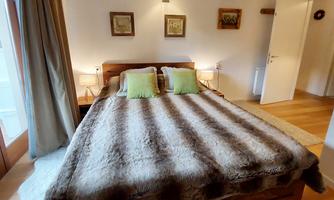 A cozy bedroom with a large bed and green pillows. The walls are decorated with pictures and there are windows that let in natural light.