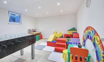 A colorful play area with toys and soft mats. There is a foosball table and a slide for children.