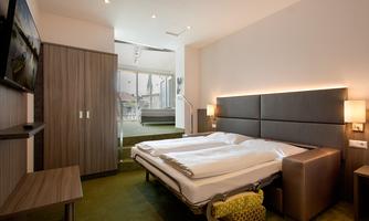 A modern bedroom with two beds, a television, and stylish furniture. The room has a bright atmosphere with large windows and carpet flooring.