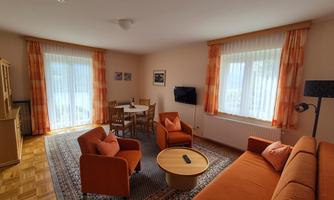 A cozy living room with orange furniture and large windows. The room is bright and inviting, perfect for relaxing.