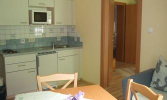 A bright kitchen with modern appliances and a dining table. In the background, a living room with a couch can be seen.