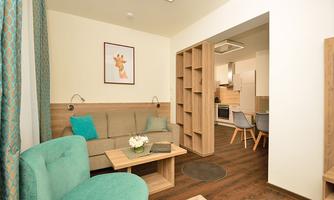 A modern living room with a comfortable sofa and stylish furniture. In the background, there is an open kitchen with a dining area.