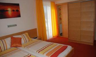 A cozy bedroom with two beds and colorful cushions. Large windows let in plenty of daylight, and the walls are designed in warm colors.