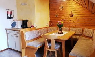 A cozy kitchen with a wooden chair and a large table. Decorations hang on the wall, and a bouquet of flowers is on the table.