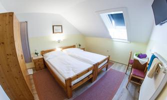 A cozy bedroom with two beds and a desk. The room features a skylight and warm wooden furniture.