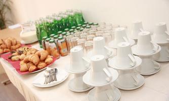 A buffet with drinks, croissants, and pastries. On the table, white cups and spoons are arranged along with various bottles.