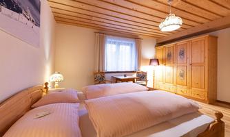 A cozy bedroom with a wooden ceiling and two beds. The room is bright and cheerfully furnished, ideal for a relaxing stay.