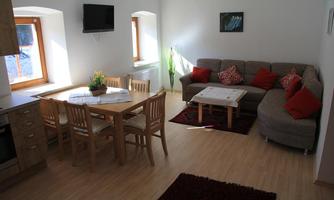 A bright living room with a cozy couch and a wooden dining table. Large windows bring plenty of daylight into the room.