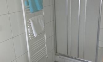 A modern bathroom with a shower cubicle and a towel rack. The walls are brightly tiled, and the floor is bluish.
