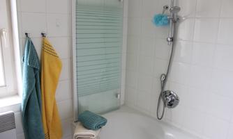 A bathroom with a bathtub and a shower. Colorful towels hang on the wall and the room is bright and clean.
