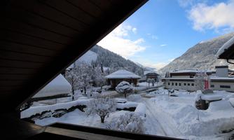 A wintry view of snow-covered mountains and houses. The sky is clear with a few clouds, and the landscape appears calm and peaceful.