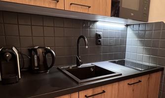 A modern kitchen with wood paneling and black surfaces. There is a sink, a kettle, and a microwave.