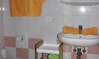 A bright bathroom with orange towels and a sanitary fixture. There is a sink with a shelf and an orange basket for towels.