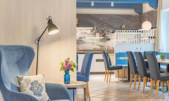 An inviting room with blue armchairs and a table. The room is bright and modernly decorated, with a floral arrangement and appealing lighting.