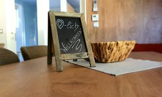 A small wooden stand with a sign that says "Welcome." In the background, a wooden bowl and part of the living space can be seen.