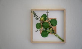 A beautiful wall painting featuring fresh plants in a wooden frame. The green leaves and the soft background create a calming atmosphere.