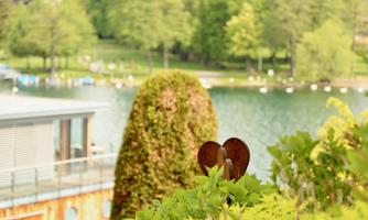 A beautiful garden scene with a heart-shaped decorative piece and green plants. In the background, there is a tranquil lake and trees.