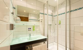 A modern bathroom with a shower and a washbasin. The walls are brightly tiled and there is a large mirror.