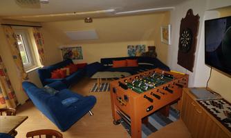 A cozy room with blue sofas and orange pillows. There is a foosball table and a television on the wall.