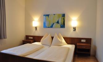 A cozy bedroom with a double bed and modern nightstands. The walls are bright, and a colorful painting beautifies the space.
