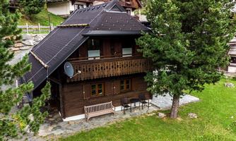 A beautiful wooden house with a black roof. It is surrounded by trees and grass in a quiet environment.