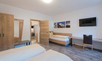 A cozy room with two beds, a desk, and a television. The walls are light, and there are wood details as well as pictures on the wall.