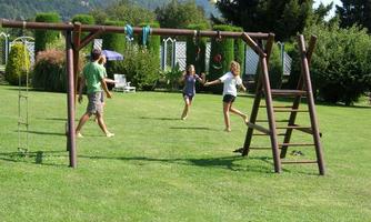 A sunny garden with a playground. Children are playing and running over the green meadow.