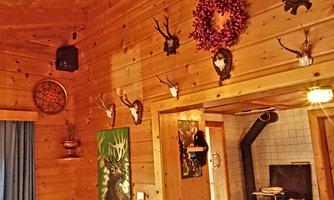 A rustic wooden wall adorned with hunting trophies and decorative wreaths. To the right, a wooden stove is visible, creating a cozy atmosphere.