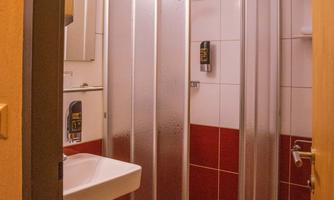 A small bathroom with a shower cubicle and a sink. The walls are tiled in white, and a red accent adds color.