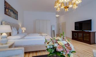 A modern bedroom with a large bed, elegant lamps, and a stylish television. A floral table decoration complements the cozy atmosphere.