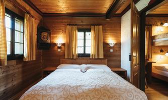 A cozy bedroom with wooden decor and warm light. The bed is inviting and the windows let in daylight.
