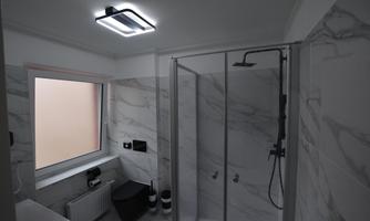 A modern bathroom with a shower and marble walls. There is a window and elegant ceiling lighting.