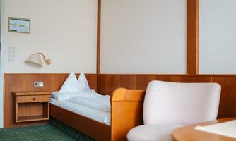 A simple hotel room with a bed, an armchair, and a table. The walls are in warm wood and pastel tones.